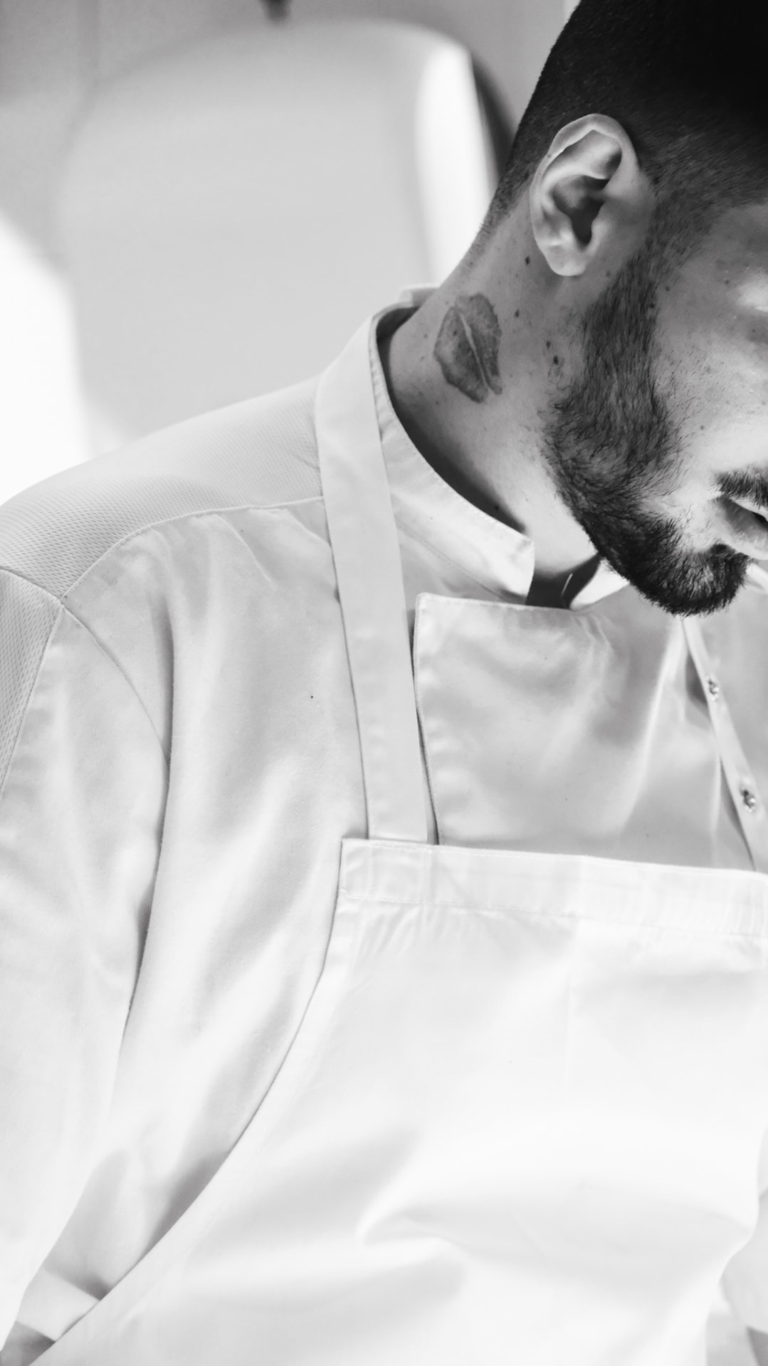 Chef in whites and apron, head lowered, black and white portrait