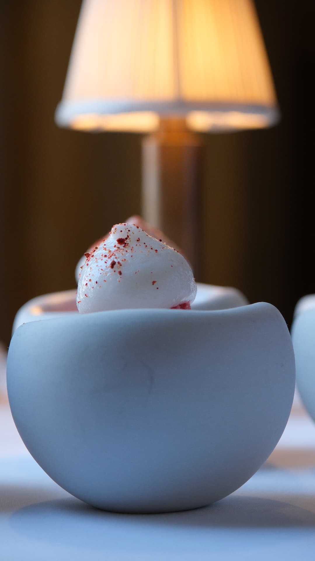 Dessert with a quenelle of cream dusted in red, lit by a table lamp