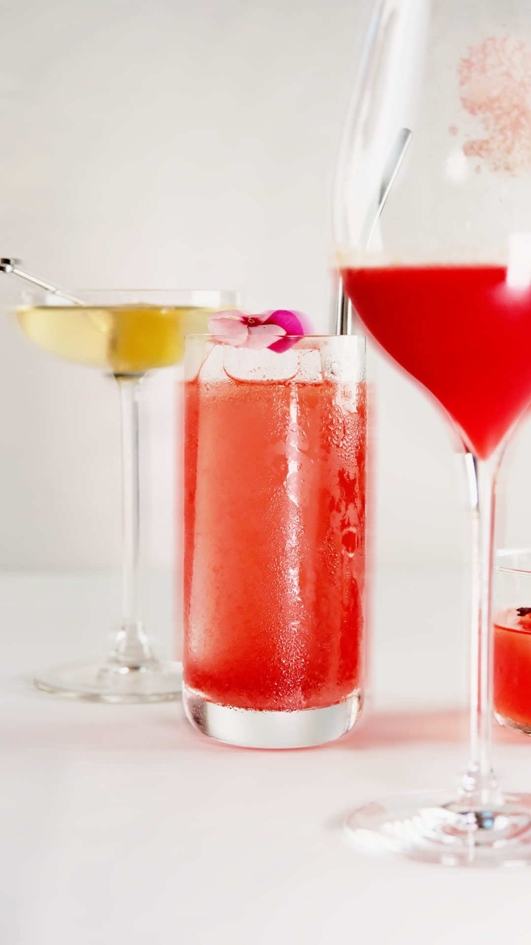 Three cocktails on white, one with a pink blossom on ice